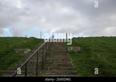 Betontreppe auf einem Deich mit einem Eisengeländer Der mittlere und ein wolkig Himmel Stockfoto