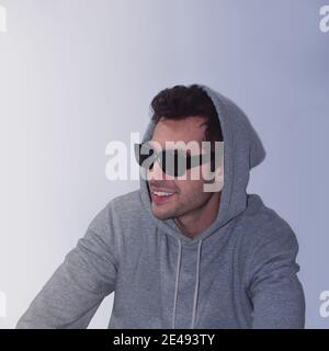 Stilvoller und hübscher junger Mann mit grauem Hoodie und Schwarze Sonnenbrille auf weißem Hintergrund Stockfoto