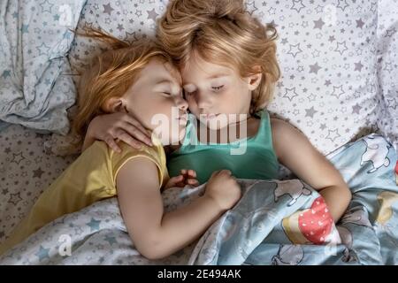 Zwei kleine Geschwister Mädchen Schwestern schlafen in einer Umarmung im Bett unter einer Decke. Stockfoto