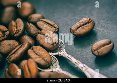 Vintage Hintergrund von gerösteten Kaffeebohnen mit Löffeln auf dunklem Hintergrund, selektiver Fokus, Stimulans von Energie-Konzept Stockfoto