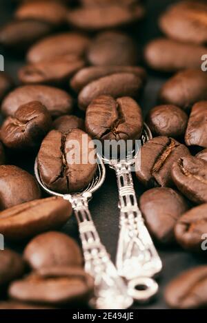 Geröstete Kaffeebohnen in zwei Löffeln, selektiver Fokus. Kaffeepause-Konzept. Vertikaler Vintage-Hintergrund Stockfoto