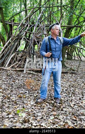 Weißhaarige, kaukasische Männer tragen Hosenträger, Baskenmütze und blaue Jeans i Hölzer vor einer Festung aus Zweigen Stockfoto