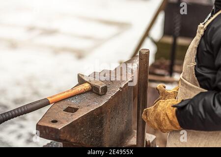 Der Junge, der Sohn des Schmieds, steht am Amboss. Der Prozess des Schmiedens. Stockfoto