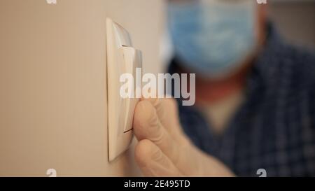 Mann trägt medizinische Maske und Schutzhandschuhe Betreten Sie den Büroraum und schalten Sie das Licht aus dem Schalter, Arbeitsplatz Quarantäne in Pandemie. Stockfoto