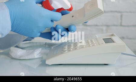 Mann trägt Schutzhandschuhe in den Händen Reinigung und Desinfektion eines Telefons mit einem Spray und feuchten Wischtüchern Stockfoto