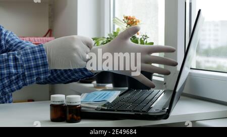 Kranker Mann mit einem Laptop auf die Hände legen Schutzhandschuhe, sozialer distanzierender Lebensstil in Pandemic Periode Stockfoto