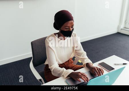 Frau, die am Laptop arbeitet und eine Gesichtsmaske trägt Stockfoto