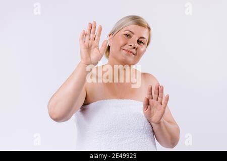Eine ältere Frau in ein weißes Handtuch gewickelt mit einem Lächeln posiert und zeigt gesunde und mit Feuchtigkeit versorgt weiche Hände auf einem weißen Hintergrund. Stockfoto