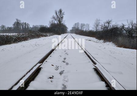 Schneebedeckte Bahngleise mit Fußspuren, die an einem kalten Wintertag in die Ferne führen. Stockfoto