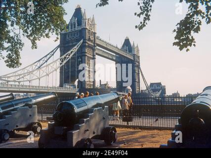 1974 Tower Bridge London - Touristen, die vor dem Tower of London an Kanonen vorbeilaufen in der Nähe der Tower Bridge London - Tower Bridge ist eine kombinierte Bascule- und Hängebrücke in London, die zwischen 1886 und 1894 erbaut wurde. Die Brücke überquert die Themse in der Nähe des Tower of London und ist zu einem weltberühmten Wahrzeichen Londons geworden. London Tower Bridge und Themse City of London England GB Großbritannien Europa Stockfoto