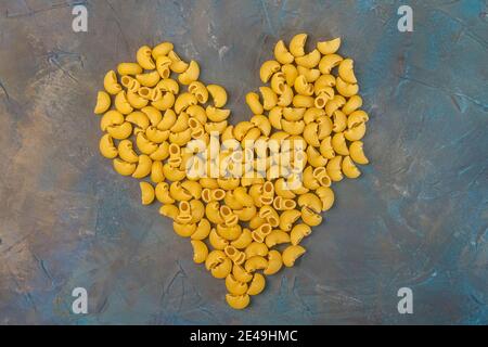 Rohe Ellenbogen Pasta in Form von Herz liegt auf einem launisch dunklen Hintergrund. Das Konzept des Valentinstag Stockfoto