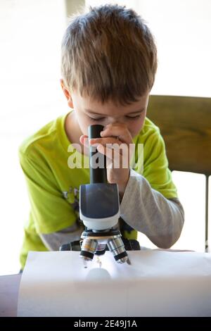 Nahaufnahme eines Jungen, der durch ein Mikroskop auf einen schaut Fehler Stockfoto