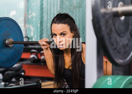 Weibliche Sportlerin, die beim Heben des Gewichts im Freien auf die Kamera schaut Fitnessraum Stockfoto