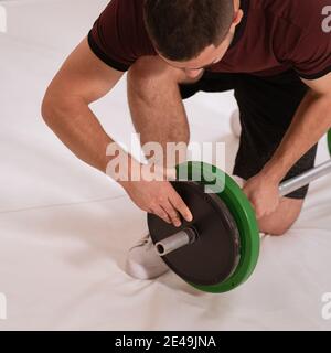 Hinzufügen von Gewicht zu einer Langhantel jungen Mann Bogen auf einem Knie wechselnden schwarzen und grünen Platten, Ausrüstung für Krafttraining Konzept. Sportausrüstung für Stockfoto