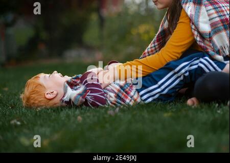 Ältere Schwester kitzelt kleinen Bruder im Gras draußen in Eine Decke Stockfoto