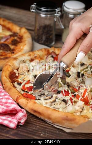 Frauenhand schneidet die Pizza mit einem Pizzabesser. Hausgemachte Pizza. Lieferung nach Hause. Stockfoto