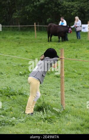 Straiton, Ayrshire, Schottland, Großbritannien 10. Juni 2017. Lokale landwirtschaftliche Show. Kleines Mädchen in Reitkleidung lehnt sich an Seil suchen gelangweilt und satt ! Stockfoto