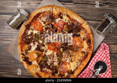 Draufsicht auf eine frisch gekochte Pizza in einer Pappschachtel, Pizzabesser auf einer Serviette und Salz und Pfeffer auf einem Holztisch. Pizzalieferung. Essen Sie zu Hause. Stockfoto