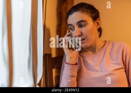 Überraschte Frau, die am Fenster telefoniert Stockfoto