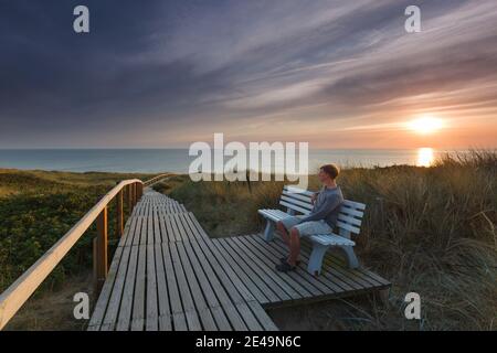 Kurz vor Sonnenuntergang sitzt eine Person auf einer Bank am Strandübergang in Rantum auf der Insel Sylt in Nordfriesland, Schleswig-Holstein, Deutschland Stockfoto