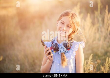 Grillendes Teenager-Mädchen mit Kopfhörern, die das Smartphone in der Hand halten Auf Sunshine Field Hintergrund Stockfoto