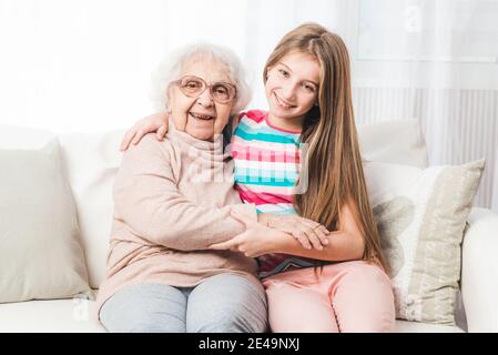 Lächelnde Enkelin sitzt umarmt mit Großmutter Stockfoto