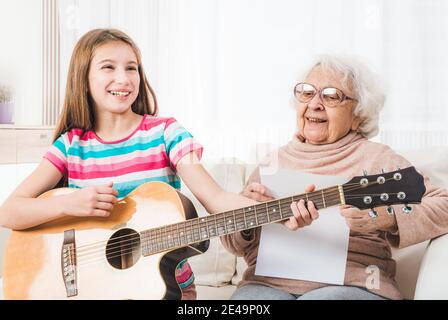 Lächelnde Enkelin spielt auf der Gitarre für Großmutter Stockfoto