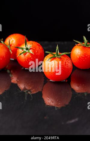 Nahaufnahme von feuchten Kirschtomaten, auf nassem Schiefer, mit Spiegelung, schwarzer Hintergrund, vertikal, mit Kopierraum Stockfoto