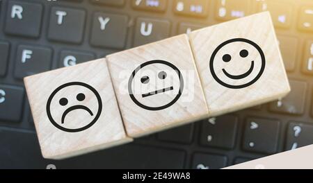 Smiley-Bewertung. Stirnrunzeln, neutrales und glückliches Gesicht auf Holzblöcken Spielzeug auf Computer-Tastatur. Bewertungskonzept. Stockfoto