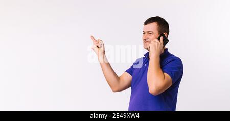 Banner, Langformat. Ein netter Mann mit blauem T-Shirt spricht am Telefon und zeigt mit seinem Zeigefinger auf einen leeren weißen Raum. Grau Stockfoto