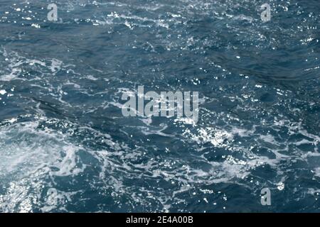 Wellen auf dem Meer. Meerwasseroberfläche und -Spritzer, Dunkelblaues Meerwasser für natürlichen Hintergrund. Von oben nach unten Luftaufnahme der Meerwasseroberfläche. Weißer Schaum Stockfoto
