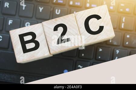 B2C auf einem Holzwürfel vor einem Laptop geschrieben. Business-to-Customer-Konzept. Stockfoto