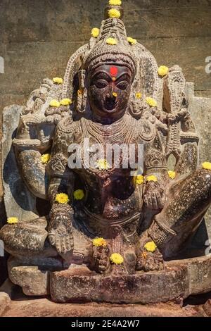 Lakkundi, Karnataka, Indien - 6. November 2013: Brahma Jinalaya Tempel. Beschädigte Vishnu schwarzen Stein Vishnu Statue mit gelben Blumen. Stockfoto