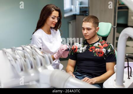 Portrait einer jungen Zahnärztin, die bei einem mittleren Erwachsenen in der Klinik steht. Weibliche Zahnarzt Reparatur Patienten Zahn in zahnärztlichen ambulant Stockfoto