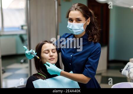 Die schöne junge Frau ist beim Zahnarzt. Sie sitzt auf dem Zahnarztstuhl und der Zahnarzt untersucht sorgfältig die Zähne des Patienten. Der Zahnarzt Stockfoto