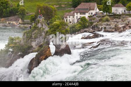 Rheinfall, Schweiz - 6. Mai 2017: Rheinfalllandschaft bei bewölktem Frühlingstag sind Touristen auf kleinen Felsen und an der Küste in der Nähe Stockfoto