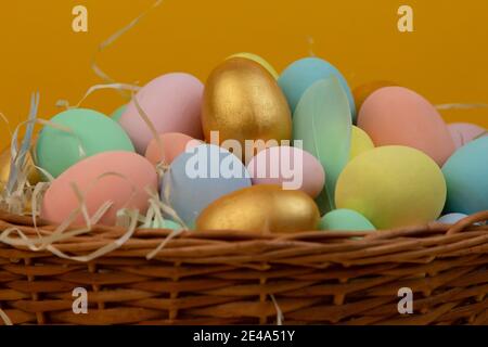 Korbkorb mit bunten Ostereiern in Pastellfarben auf Gelber Hintergrund Stockfoto