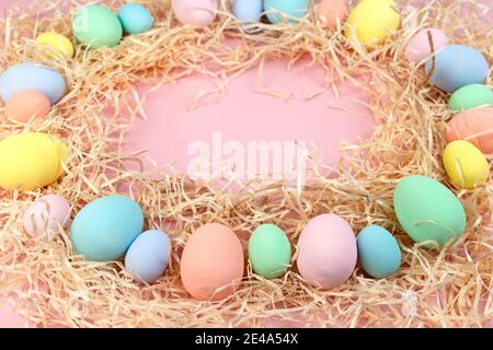 Mehrfarbige Ostereier und Federn in Pastellfarben liegen auf Spänen in Form eines Rahmens. Festliche Osterkarte. Stockfoto