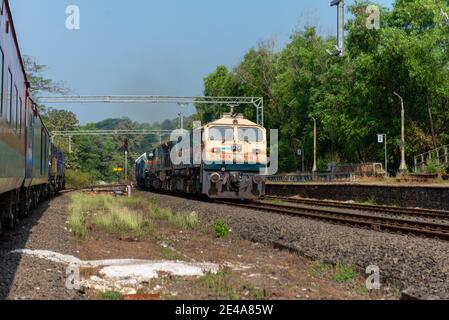 Güterzug Kreuzung 02413 Madgaon - Delhi Hazrat Nizamuddin Rajdhani Special an schönen malerischen Pernem Bahnhof auf Konkan Railway. Stockfoto