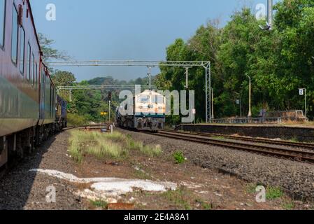 Güterzug Kreuzung 02413 Madgaon - Delhi Hazrat Nizamuddin Rajdhani Special an schönen malerischen Pernem Bahnhof auf Konkan Railway. Stockfoto