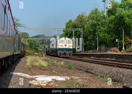 Güterzug Kreuzung 02413 Madgaon - Delhi Hazrat Nizamuddin Rajdhani Special an schönen malerischen Pernem Bahnhof auf Konkan Railway. Stockfoto