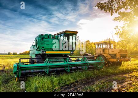 Der moderne grüne Mähdrescher und gelbe Schwerlasttraktor Auf landwirtschaftlichem Feld in den Strahlen der Herbstsonne Stockfoto
