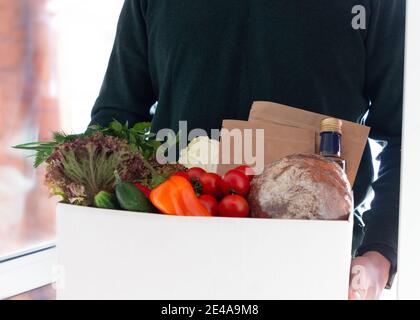 Eine Person, die Box mit Landwirt Bio-Ernte in der Tür des Hauses. Frische Bio-Gemüse und Lieferung von Gemüse. Support für kleine Unternehmen vor Ort. Stockfoto