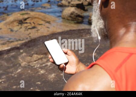 Senior african american Mann trägt Kopfhörer mit Smartphone von der Meer Stockfoto