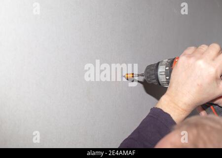 Ein Mann verwendet einen Schraubendreher, um eine Schraube in eine Trockenwand zu Schrauben. Renovierung des Hauses, Wandverkleidung. Stockfoto