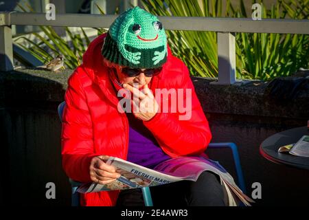 Ältere Frau liest Zeitung, trägt Froschhut. Stockfoto