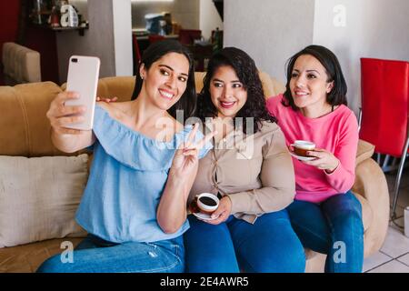 Lateinamerikanische Freundinnen, die ein Selfie-Foto machen und Kaffee trinken Zu Hause in Mexiko-Stadt Stockfoto