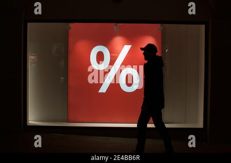 Beleuchtetes rotes Prozent-Verkaufsschild in einem Schaufenster mit einem nicht erkennbaren Mann, der in der Stadt Lugano, Schweiz, vorbeikommt. Stockfoto