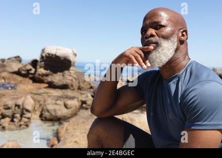Fit Senior african american Mann sitzt auf felsigen Küste denken. Gesunde Ruhestand Outdoor Fitness-Lifestyle. Stockfoto