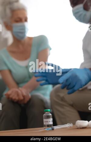 Senior african american männlichen Arzt Vorbereitung covid 19 Impfung für ältere kaukasische Frau zu Hause. Gesundheit und Hygiene zu Hause in Selbstisolatio Stockfoto